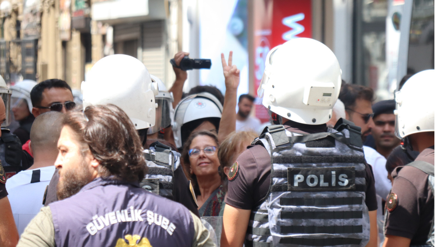 polis ablukasından objektife doğru zafer işareti yapan bir hak savunucusu görünüyor