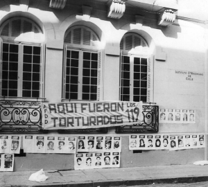 this photograph from 1980 shows a banner reading “Aquí fueron torturados los 119 / 119 people were tortured here” hung on the building that was used as O’Higgins Institute for Military Research at the time.
